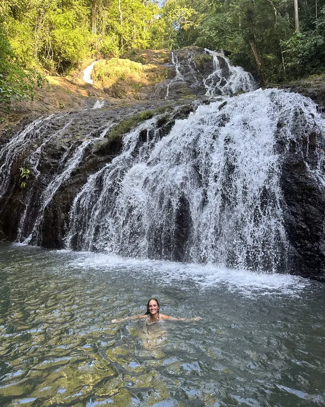 Two swimmers in the pool beneath a wide waterfall