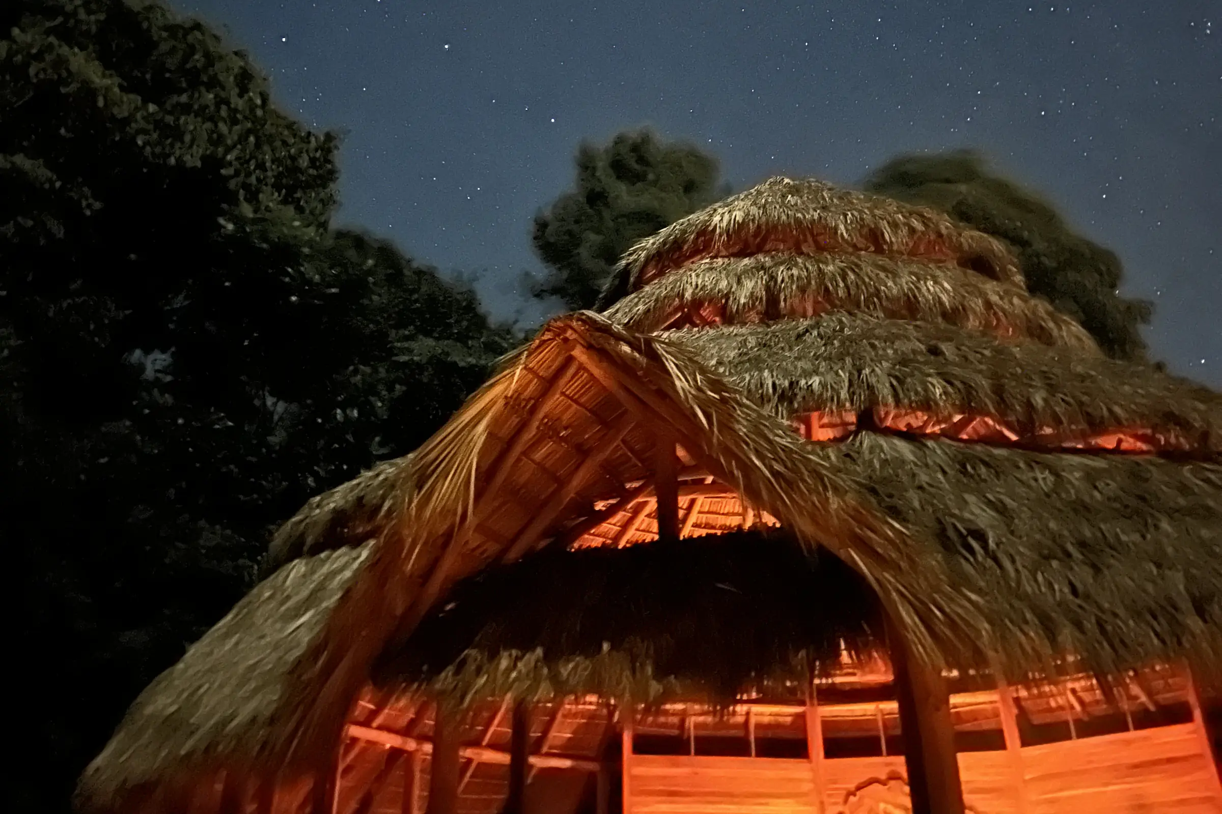 The Maloca lit from within beneath a sky full of stars