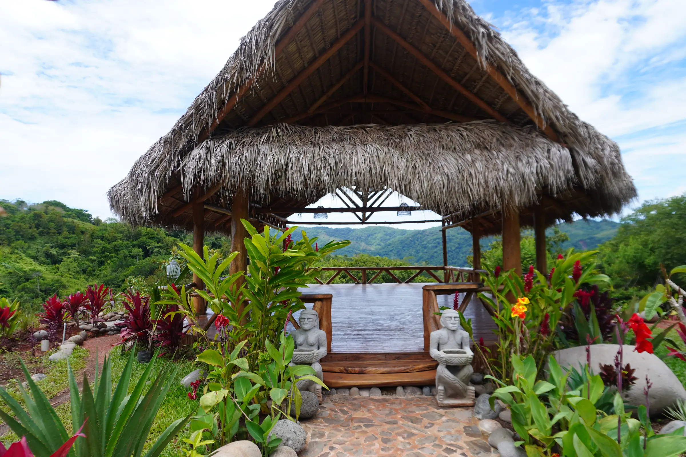 The entrance to the yoga shala, between flowers and stone statues, with the mountains beyond